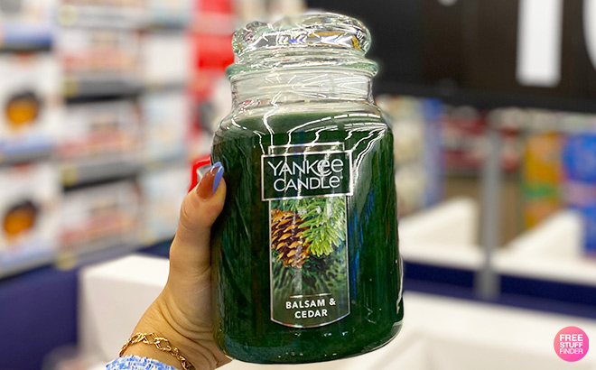 Hand holding a Yankee Candle Balsam Cedar in a store aisle