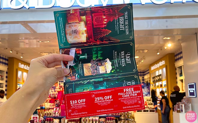 Hand holding one Bath and Body Works Open Pamphlet with coupons