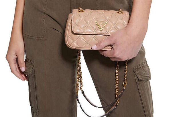Woman is Holding Guess Giully Mini Convertible Crossbody Bag in Apricot Cream Color