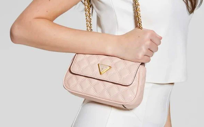 Woman is Holding Guess Giully Mini Convertible Flap Quilted Crossbody Bag in Apricot Cream Color