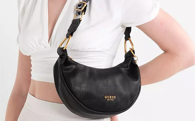 Woman is Holding Guess Natalya Small Faux Leather Hobo Bag in Black Color 