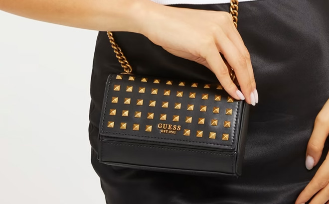 Woman is Holding a Guess Iseline Studded Mini Chain Crossbody Flap in Black Color