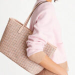 Women is Holding a Tory Burch Geometric Ever Ready Small Coated Canvas Zip Tote in Winter Peach Color