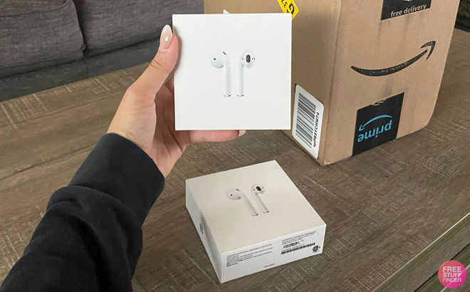 Hand Holding Apple AirPods with Amazon Box in the Background