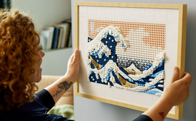 an Image of a Woman Hanging a LEGO Art Hokusai The Great Wave Building Set on a Wall