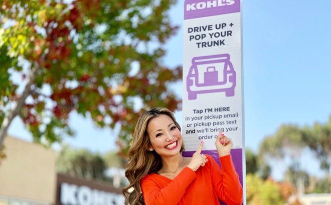 Woman Smiling and Standing Outside of a Kohl's Store Pointing to a Drive-up Sign