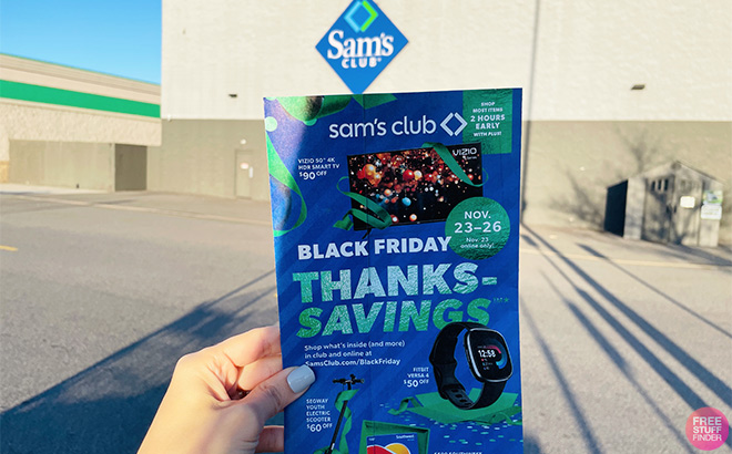 A Hand Holding the Sams Club Black Friday Ad in Front of a Sams Club Store
