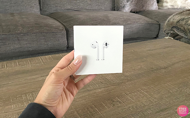 Hand Holding a Box of Apple AirPods in a Living Room