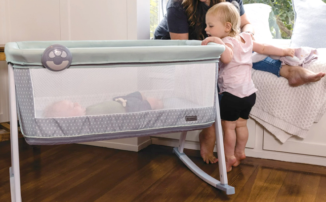Mom and Toddler Watching Over the Baby in the Monbebe Whisper Rocking Bassinet and Play Yard