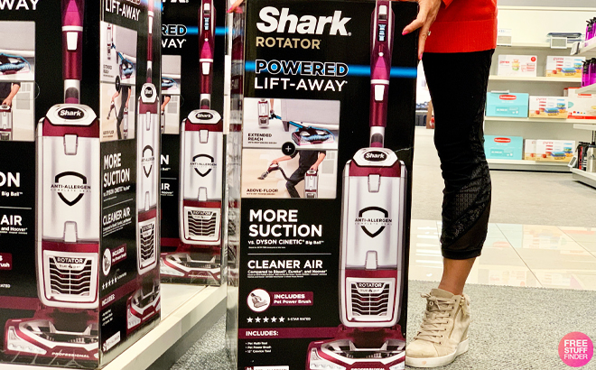 A Person Standing to a Shark Rotator Powered Lift Away TruPet Upright Vacuum in a Store Aisle