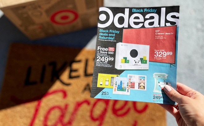 A Person Holding the Target Black Friday Ad with a Door Mat and a Box from Target in the Background