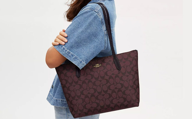 Woman is Holding Coach Zip Top Tote In Signature Canvas in Oxblood Multi Color