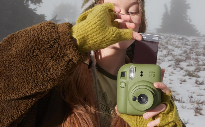 Girl is Holding Fujifilm INSTAX MINI 12 Instant Camera in Olive Color