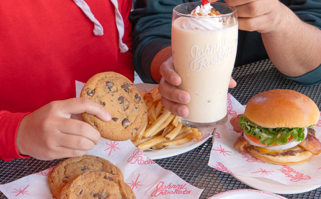 People Holding Johnny Rockets Cookies and Milkshake with a Burger and Fries on a Table