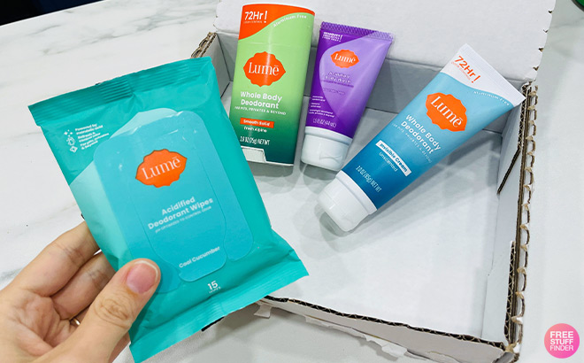 Hand Holding Lume Wet Wipes on top of Lume Products Inside a Box