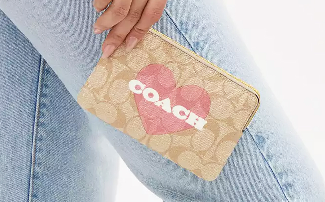 Hand Holding a Corner Zip Wristlet In Signature Canvas With Heart Print