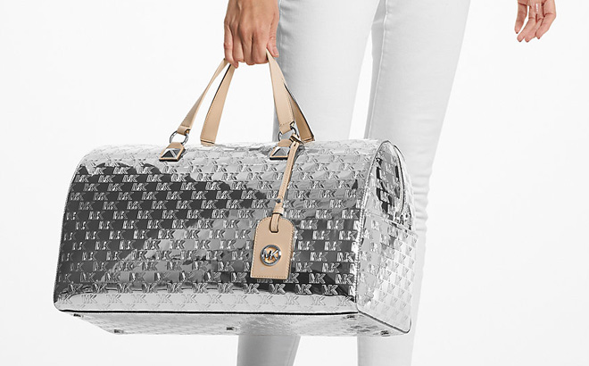 Woman is Holding Michael Kors Grayson Extra Large Logo Embossed Patent Weekender Bag in Silver Color