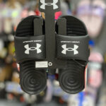 A Person Holding Under Armour Mens Ansa Fixed Slides in Black at a Store