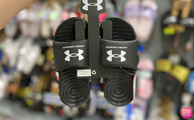 A Person Holding Under Armour Mens Ansa Fixed Slides in Black at a Store