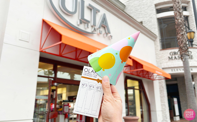 A Person Holding a Olaplex Minis Box with a Party Hat on in Front of the ULTA Store