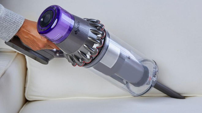 A Person Using Dyson Outsize Plus Cordless Vacuum Cleaning a Sofa