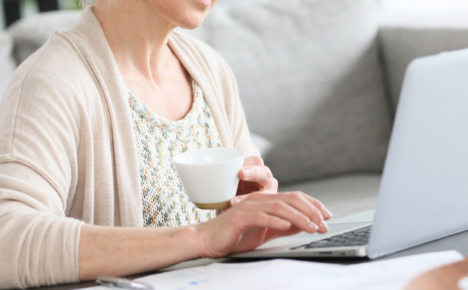 A Person Working on a Laptop and Holding a Cup of Coffee