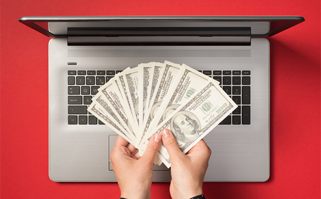 A Persong Holding Dollar Bills on Top of a Laptop with a Red Background