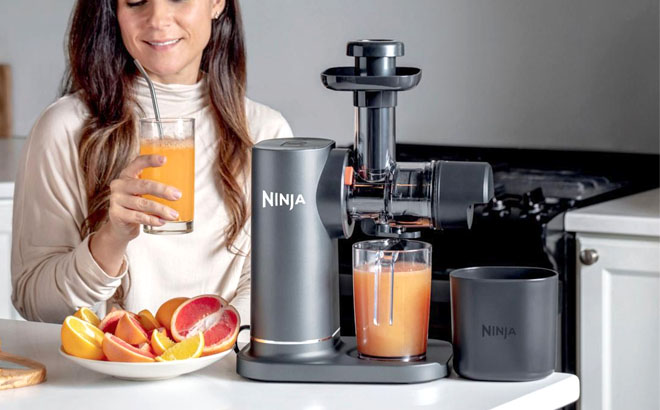 A Woman is Drinking Juice with Ninja NeverClog Cold Press Juicer on the side