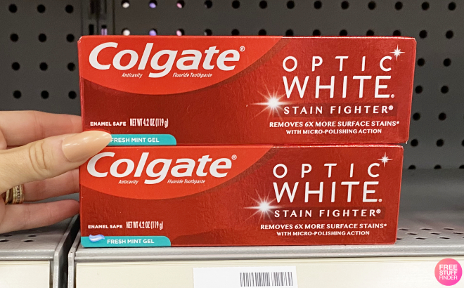 Hand Holding Colgate Optic White Stain Fighter Toothpaste on Rack