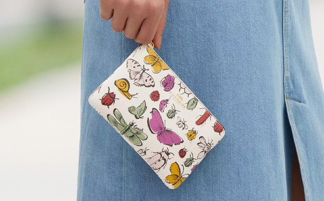 A Person Holding Coach Corner Zip Wristlet With Creature Print