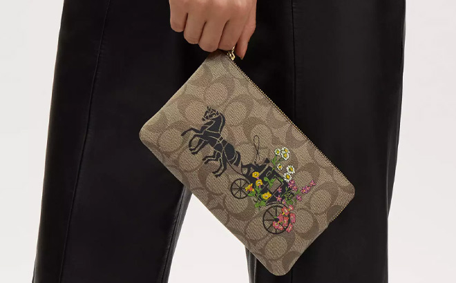 A Person Holding Coach Outlet Large Corner Zip Wristlet With Floral Horse And Carriage