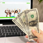 A Person Holding Money in front of Laptop