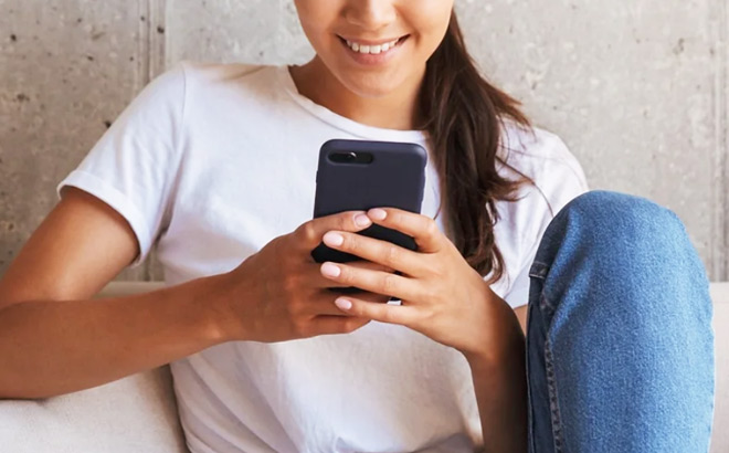A Woman Sitting on a Sofa Looking at Her Mobile Phone and Smiling