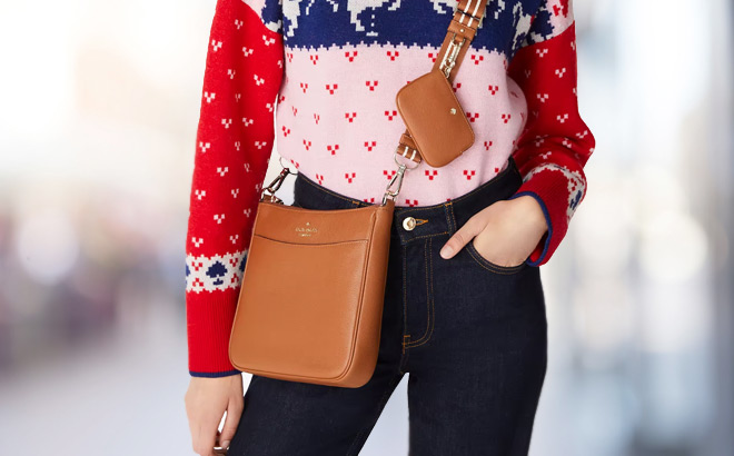 A Lady Slinging a Kate Spade Rosie Swingpack Crossbody in Warm Gingerbread Color 1