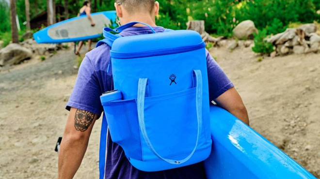 A Person Carrying a Surfboard and a Hydro Flask 20 L Carry Out Soft Cooler Pack