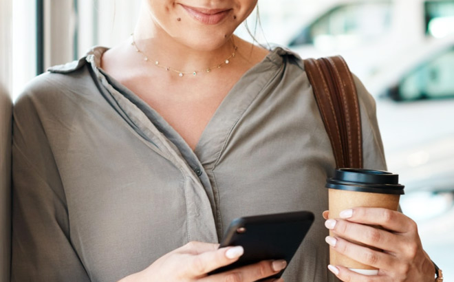 A Smiling Person Holding a Phone and a Coffee Cup while Building Their Credit A Smiling Person Holding a Phone and a Coffee Cup while Building Their Credit