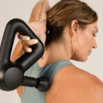 A Woman Using a Theragun Prime Massage Gun To Massager her Back