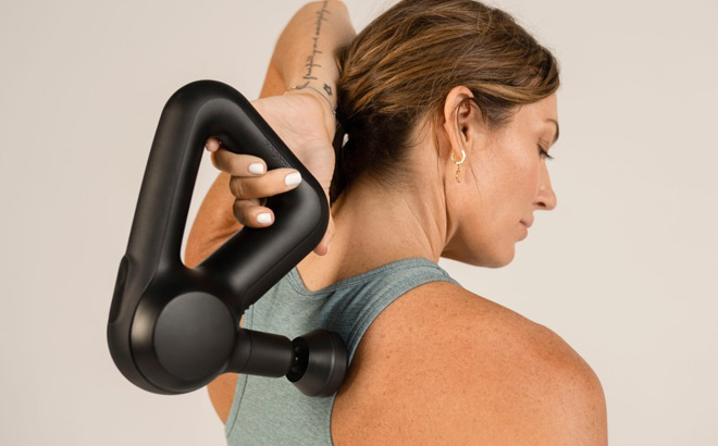 A Woman Using a Theragun Prime Massage Gun To Massager her Back