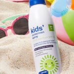 Up Up SPF 50 Kids Sunscreen Spray on a Beach Next to a Pair of Sunglasses and a Beach Ball