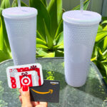 A Person Holding a Target and Amazon Gift Card with Two Lilac Starbucks Tumblers in the Background on a Table