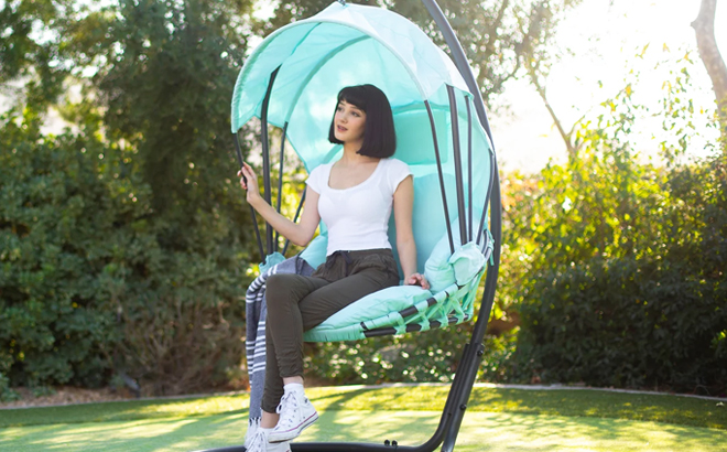 A Woman Sitting on Messer Taylors Breezy Outdoor Patio Hanging Lounge Chair in Aqua Color A Woman Sitting on Messer Taylors Breezy Outdoor Patio Hanging Lounge Chair in Aqua Color