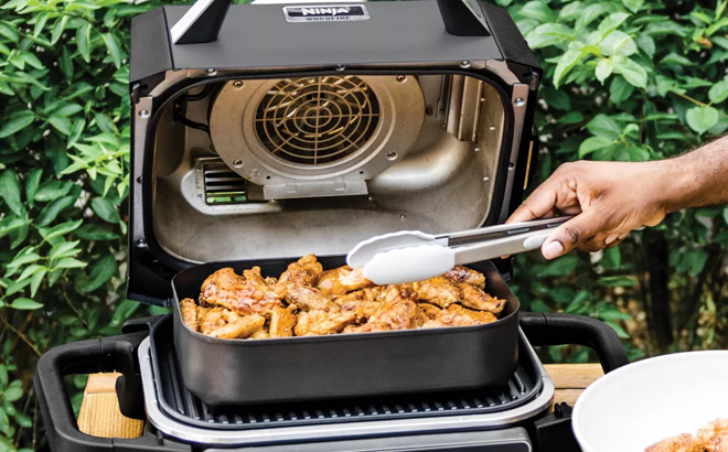 A Person getting Food out of Ninja 7 in 1 Master Outdoor Grill and Smoker A Person getting Food out of Ninja 7 in 1 Master Outdoor Grill and Smoker