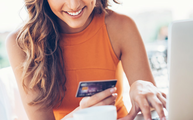 A Person Typing on a Laptop While Holding a Credit Card and Smiling A Person Typing on a Laptop While Holding a Credit Card and Smiling