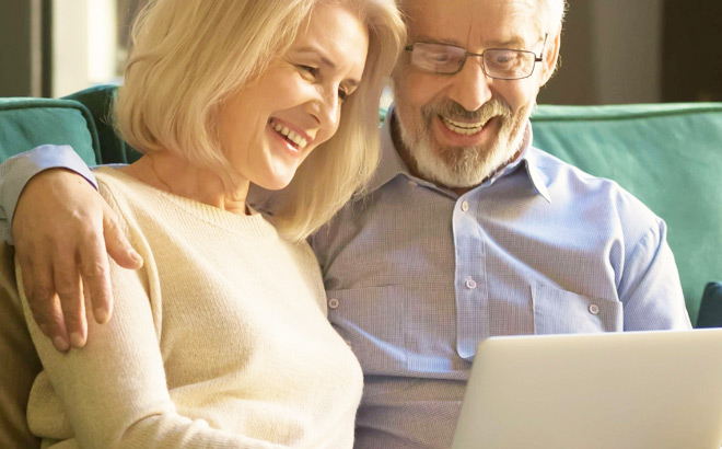 An Elderly Couple Smiling and Looking at a Laptop to Maximize Their Savings An Elderly Couple Smiling and Looking at a Laptop to Maximize Their Savings