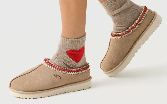 A Person Wearing UGG Tasman Slippers in the Color Sand Dark Cherry A Person Wearing UGG Tasman Slippers in the Color Sand Dark Cherry