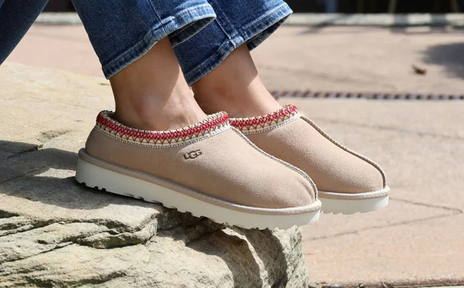 A Person Wearing the UGG Tasman Slippers in the Color Sand Dark Cherry A Person Wearing the UGG Tasman Slippers in the Color Sand Dark Cherry