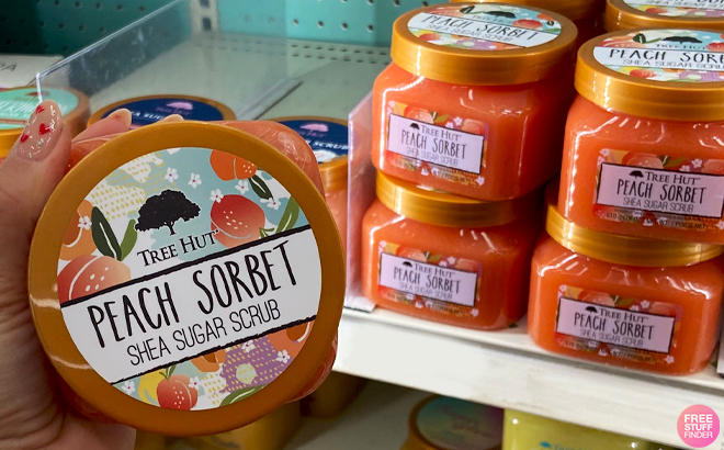 A Hand holding a Jar of Tree Hut Peach Sorbet Shea Scrub