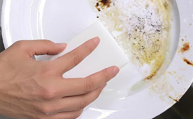 A Hand using a Magic Melamine Sponge Eraser on a Dirty Plate
