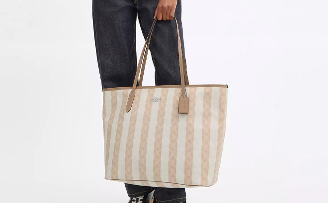 A Woman Holding Coach Outlet Large City Tote Bag In Signature Canvas with Stripe
