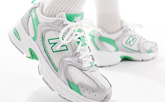 A Woman Wearing New Balance 530 Sneakers in White and Silver with Green Detailing A Woman Wearing New Balance 530 Sneakers in White and Silver with Green Detailing